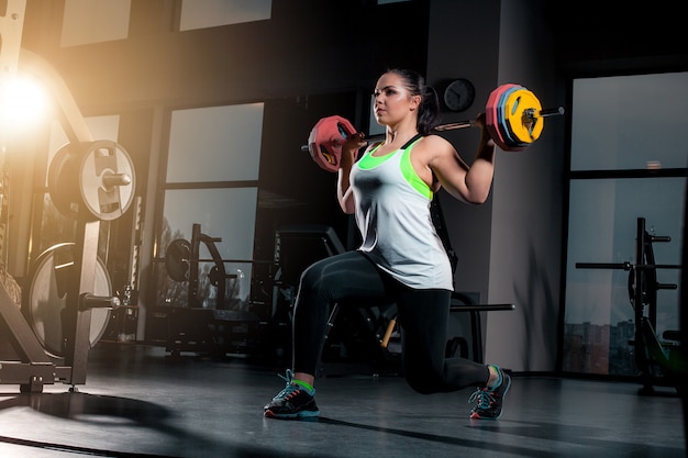 Fit jeune femme soulevant des haltères à la recherche de concentration, travaillant dans une salle de sport