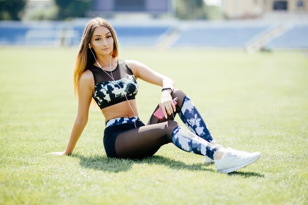 Fitness femme assise sur un tapis au stade