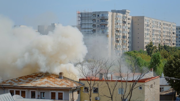Des flammes s'éteignent d'une maison en feu dans le quartier. La fumée sortant du toit en feu dans le paysage de la ville. Fumées dangereuses et smog provenant d'une explosion sortant du bâtiment détruit