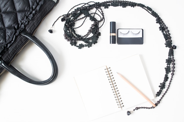 Flat lay of notebook vide, crayon et accessoires femme en concept noir, vue de dessus, isolé sur fond blanc