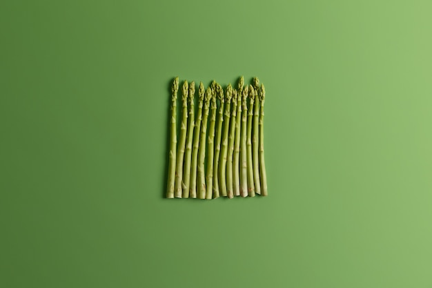 Flay lay d'asperges disposées verticalement sur fond vert. Concept de nutrition alimentaire et biologique. Vue de dessus, légumes crus frais à manger. Saison de printemps, nouvelle récolte. Ingrédient pour la cuisine