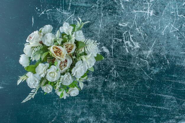 Fleur blanche artificielle dans un vase, sur fond bleu.