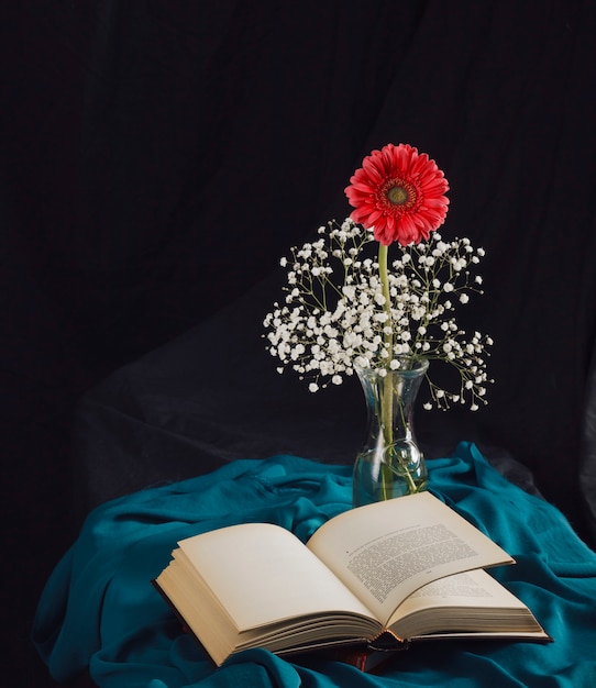Fleur avec brindilles dans un vase près du volume et textile bleu dans l&#39;obscurité