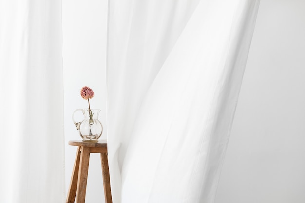 Fleur de pivoine sèche dans une cruche en verre sur un tabouret en bois dans une salle blanche