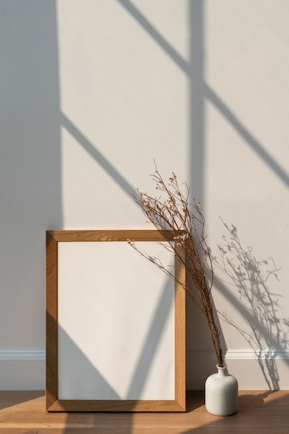 Fleur de statice blanche séchée dans un vase blanc par un cadre en bois vide sur un plancher en bois