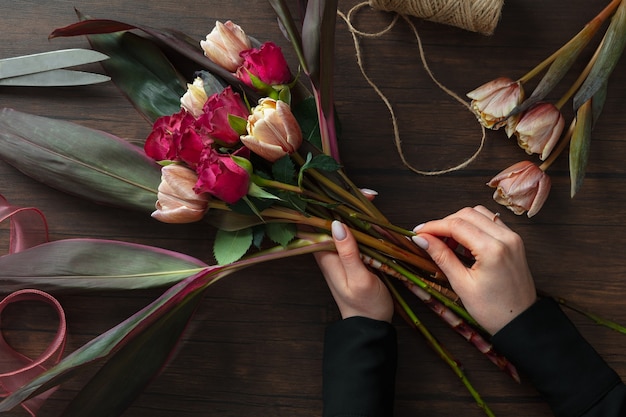 Fleuriste au travail : femme faisant un bouquet moderne de mode de différentes fleurs sur fond en bois. Cours de maître. Cadeau pour la mariée le mariage, la fête des mères, la fête de la femme. Mode printanière romantique. Roses de la passion.