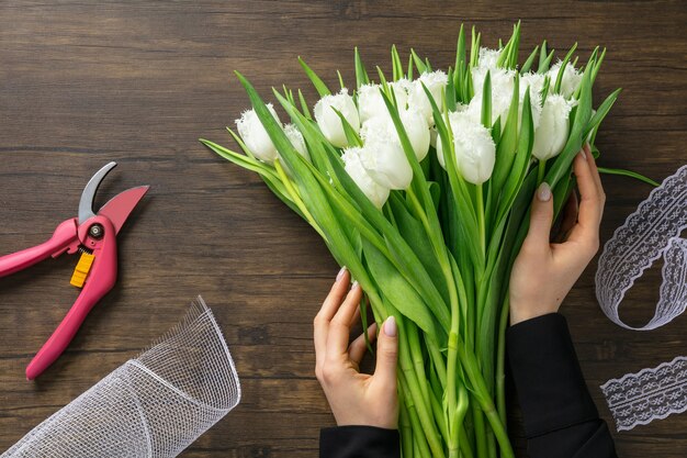 Fleuriste au travail: femme faisant un bouquet moderne de mode de différentes fleurs sur une surface en bois.