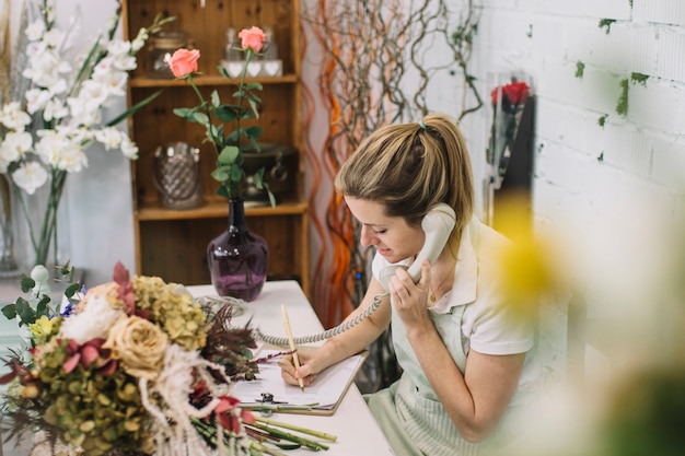 Fleuriste de charme prenant des notes pendant une conversation téléphonique