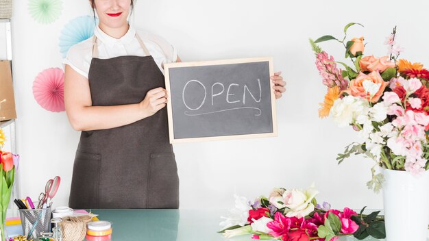 Fleuriste femme tenant en ardoise avec mot ouvert dans un magasin de fleurs