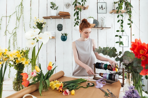 Fleuriste de jeune femme faisant le bouquet de fleurs et de rubans