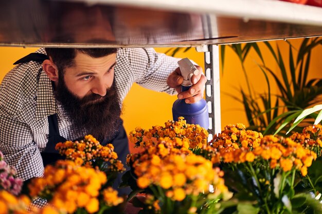 Fleuriste masculin professionnel avec barbe et tatouage sur sa main portant l'uniforme prenant soin des fleurs dans un magasin de fleurs moderne.