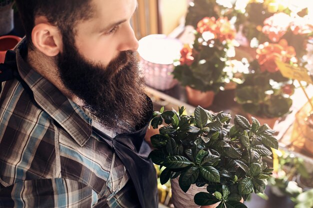 Fleuriste masculin professionnel avec barbe et tatouage sur sa main portant l'uniforme tient le pot avec un bouquet de fleurs dans un magasin de fleurs.