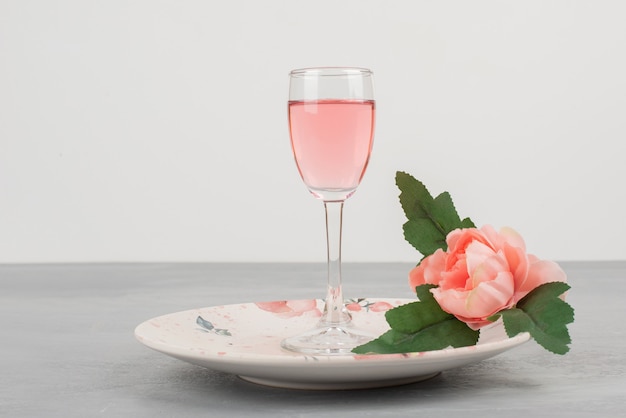 Fleurs, assiette et un verre de vin rosé sur surface grise.