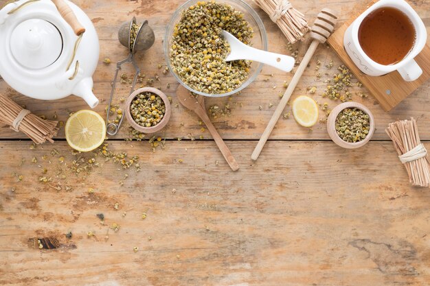 Fleurs de chrysanthème chinois séchées; théière; passoire à thé; louche de miel; contenant et thé au citron frais sur une table en bois