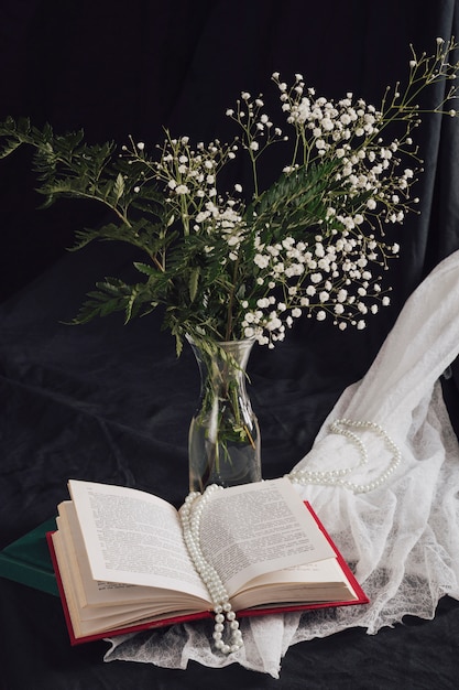 Fleurs avec des plantes dans un vase près du volume et des perles sur du textile blanc