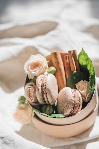 Fleurs roses avec des macarons et de la cannelle sur le récipient sur le drap blanc