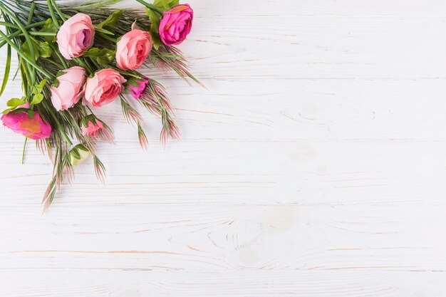 Fleurs roses roses avec des branches de plantes sur une table en bois