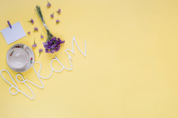 Fleurs violettes avec mot de rêve et tasse vide sur la surface jaune