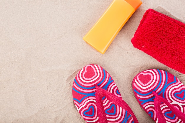 Photo gratuite flipflops, crème solaire, serviette sur la plage de sable