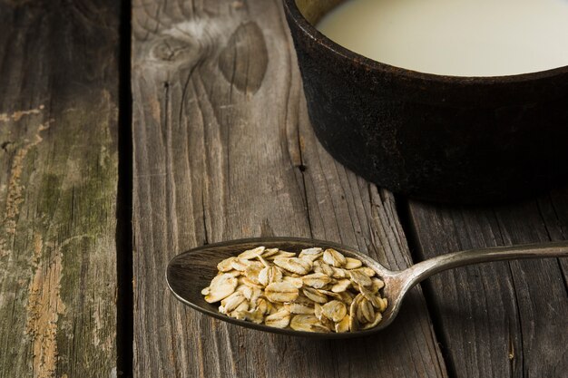 Flocons d&#39;avoine dans la cuillère rustique et le lait sur fond en bois