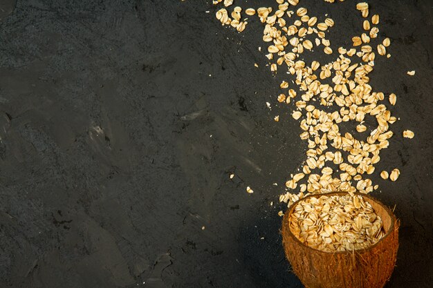 flocons d'avoine secs supérieurs renversés à partir d'une coque de noix de coco sur fond noir