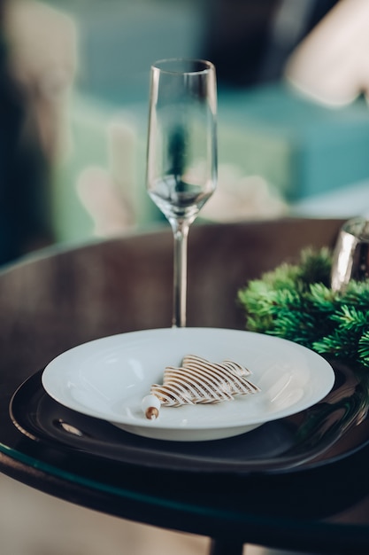 Photo gratuite flûte avec deux assiettes en porcelaine blanche et noire de taille différente sur la table servie avec branche de sapin naturel.