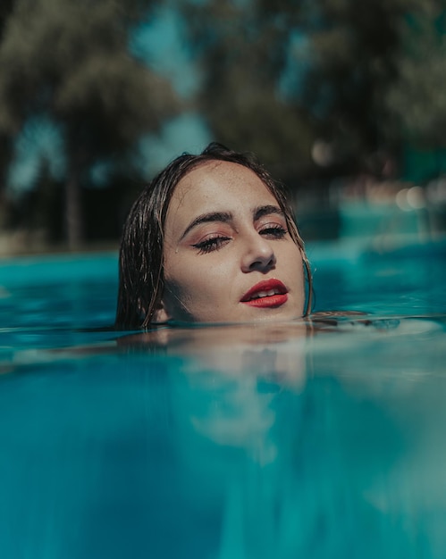 Focalisation peu profonde d'une jeune femme portant du rouge à lèvres rouge dans une piscine par une journée ensoleillée