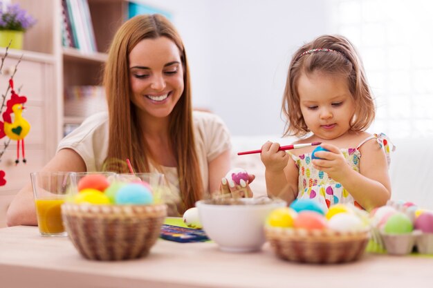 Focus petite fille peignant des oeufs de Pâques avec sa mère