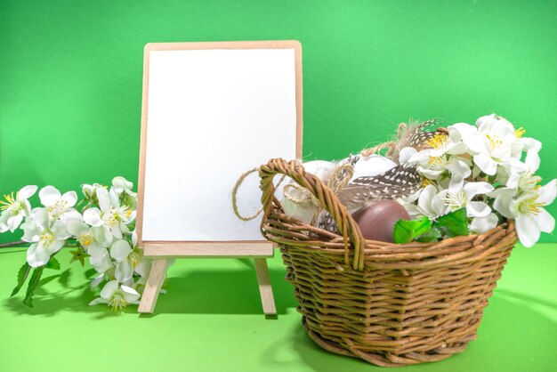Fond de carte de voeux joyeuses pâques, maquette avec des oeufs de pâques, fleurs de cerisier de printemps dans un petit panier, espace de copie de fond en bois et vert