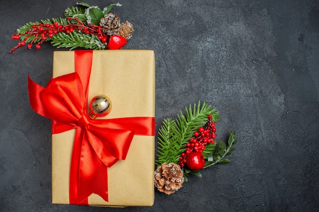 Fond de Noël avec de beaux cadeaux avec ruban en forme d'arc et accessoires de décoration de branches de sapin sur le côté droit sur une table sombre