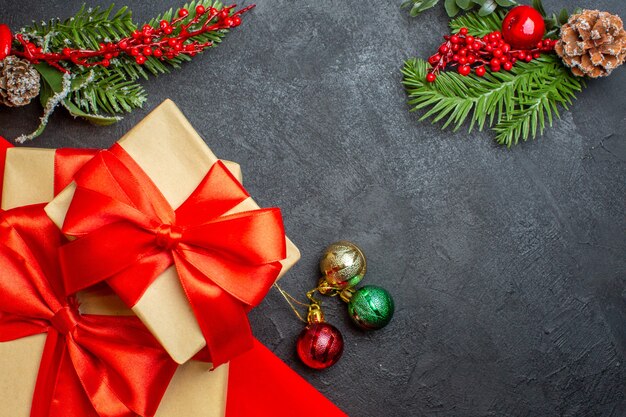 Fond de Noël avec de beaux cadeaux avec ruban en forme d'arc et accessoires de décoration de branches de sapin sur une table sombre