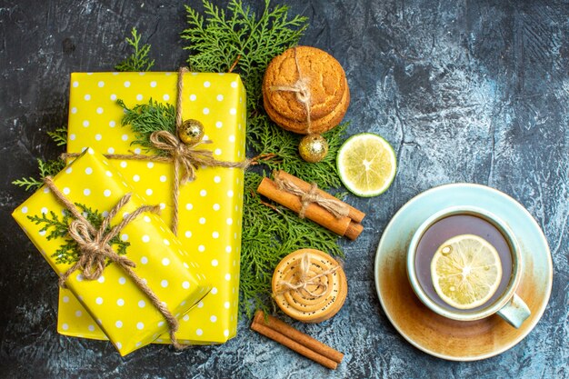 Fond de Noël avec de belles boîtes-cadeaux jaunes et des biscuits empilés citron cannelle limes à côté d'une tasse de thé noir sur fond sombre