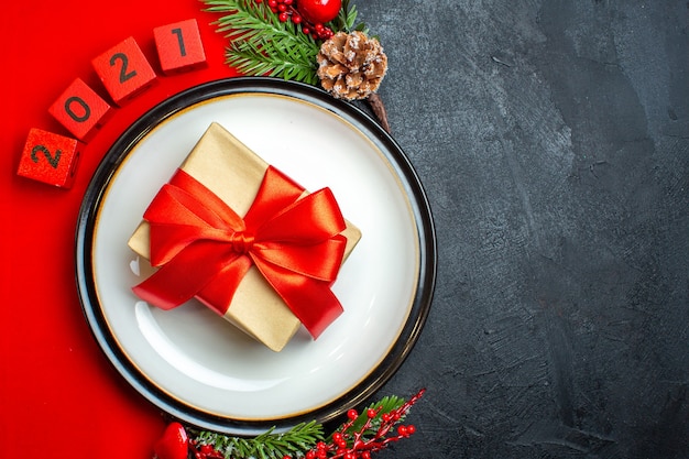 Fond de nouvel an avec beau cadeau sur une assiette à dîner accessoires de décoration branches de sapin et numéros sur une serviette rouge sur une table noire