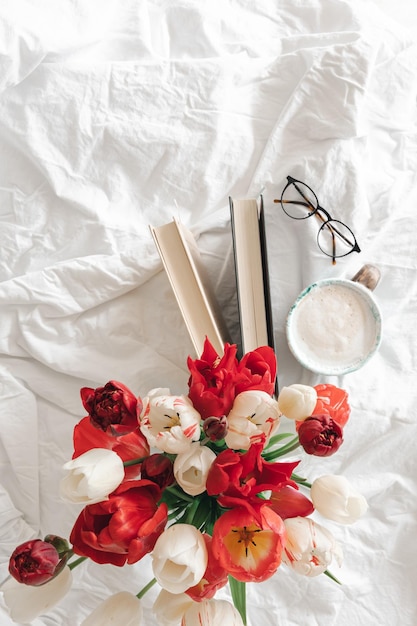 Fond de printemps avec un bouquet de tulipes une tasse de café et des livres dans un lit