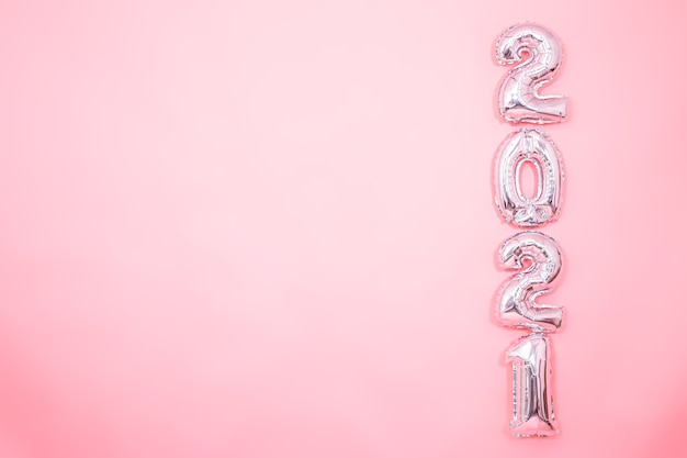 Fond rose clair avec des ballons argentés du nouvel an sous forme de chiffres sur le côté droit, concept de nouvel an