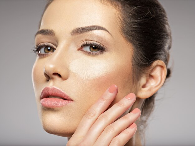 Le fond de teint de maquillage cosmétique est sur le visage de la femme. Concept de soins de la peau.