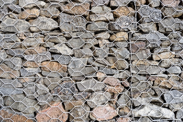 Fond texturé de Gabion, mur de roche avec clôture grillagée.