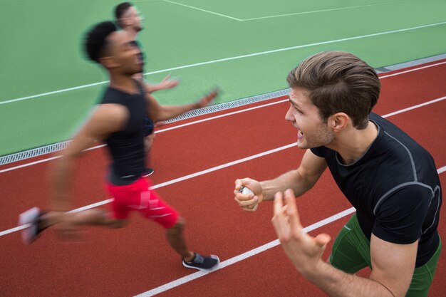 Formateur criant près de jeunes athlètes multiethniques hommes courir