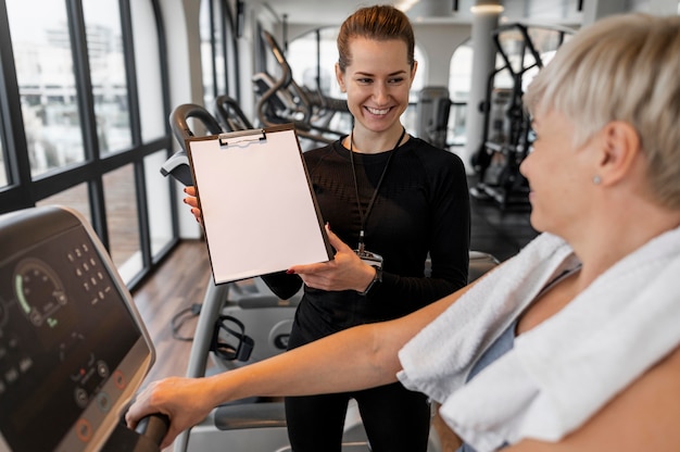 Photo gratuite formateur de programme d'entraînement et client montrant le presse-papiers