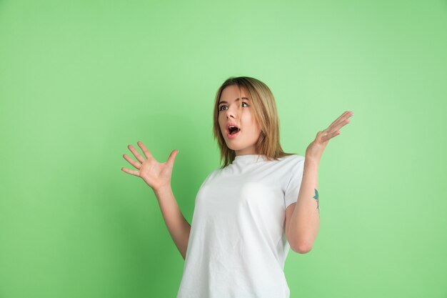 Fou choqué. Portrait de jeune femme caucasienne isolé sur mur vert. Beau modèle féminin en chemise blanche.