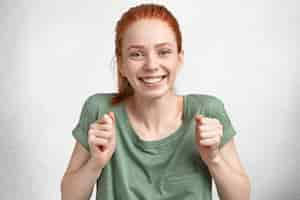 Photo gratuite fou de joie aux cheveux rouges belle jeune femme heureuse célèbre le concours gagnant, vêtu d'un t-shirt décontracté, a un large sourire, isolé sur du béton blanc