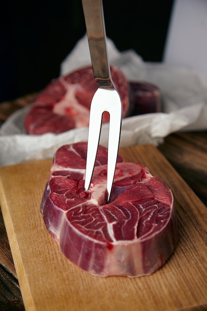 Fourchette à viande dans un steak angus. Gros plan sur table en bois, en face de steaks flous.