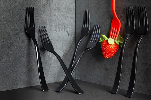 Fourchettes noires élégantes et minimalistes et une fraise sur table noire