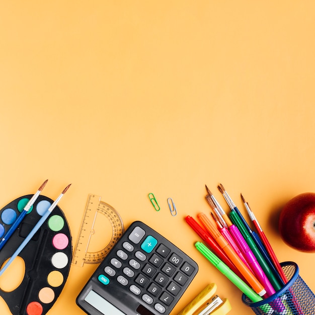 Photo gratuite fournitures scolaires multicolores et pomme rouge dispersés sur un bureau jaune