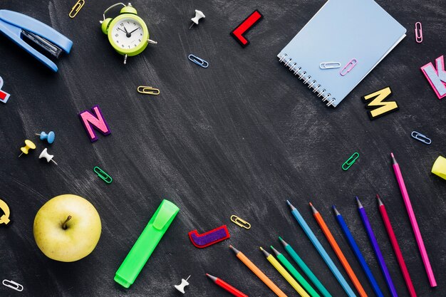 Fournitures scolaires avec pomme et réveil dispersées sur un tableau noir