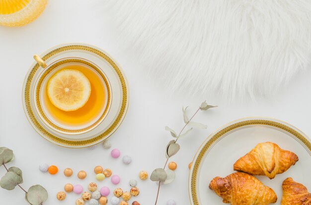 Fourrure; croissant cuit au four; bonbons et tasse de thé de citron au gingembre sur fond blanc