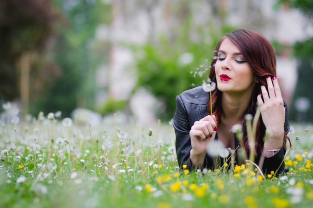 Photo gratuite foyer peu profond d'une jeune femme élégante allongée dans un parc et soufflant un pissenlit