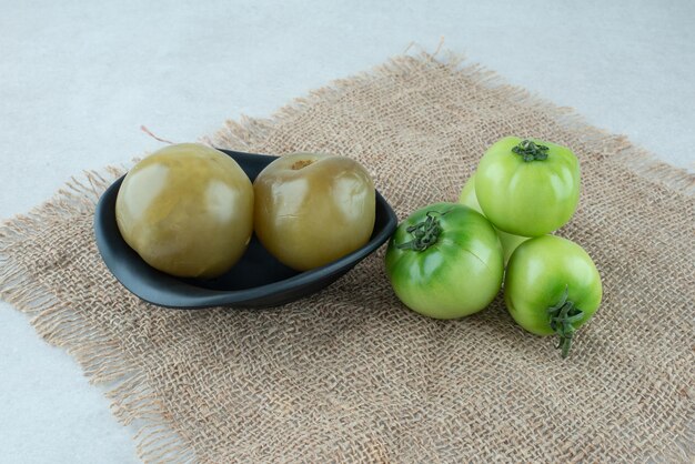 Frais et bol de tomates vertes marinées sur toile de jute.