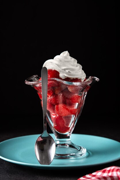 Fraises et crème fouettée dans un verre de crème glacée sur fond noir