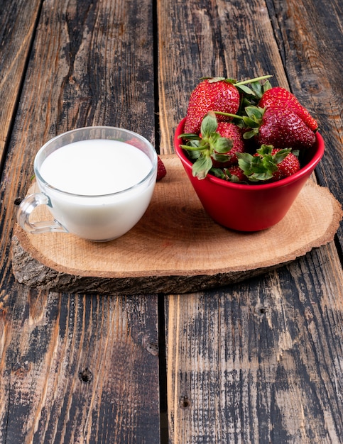 Photo gratuite fraises dans un bol avec une tasse de lait sur un talon et une table en bois